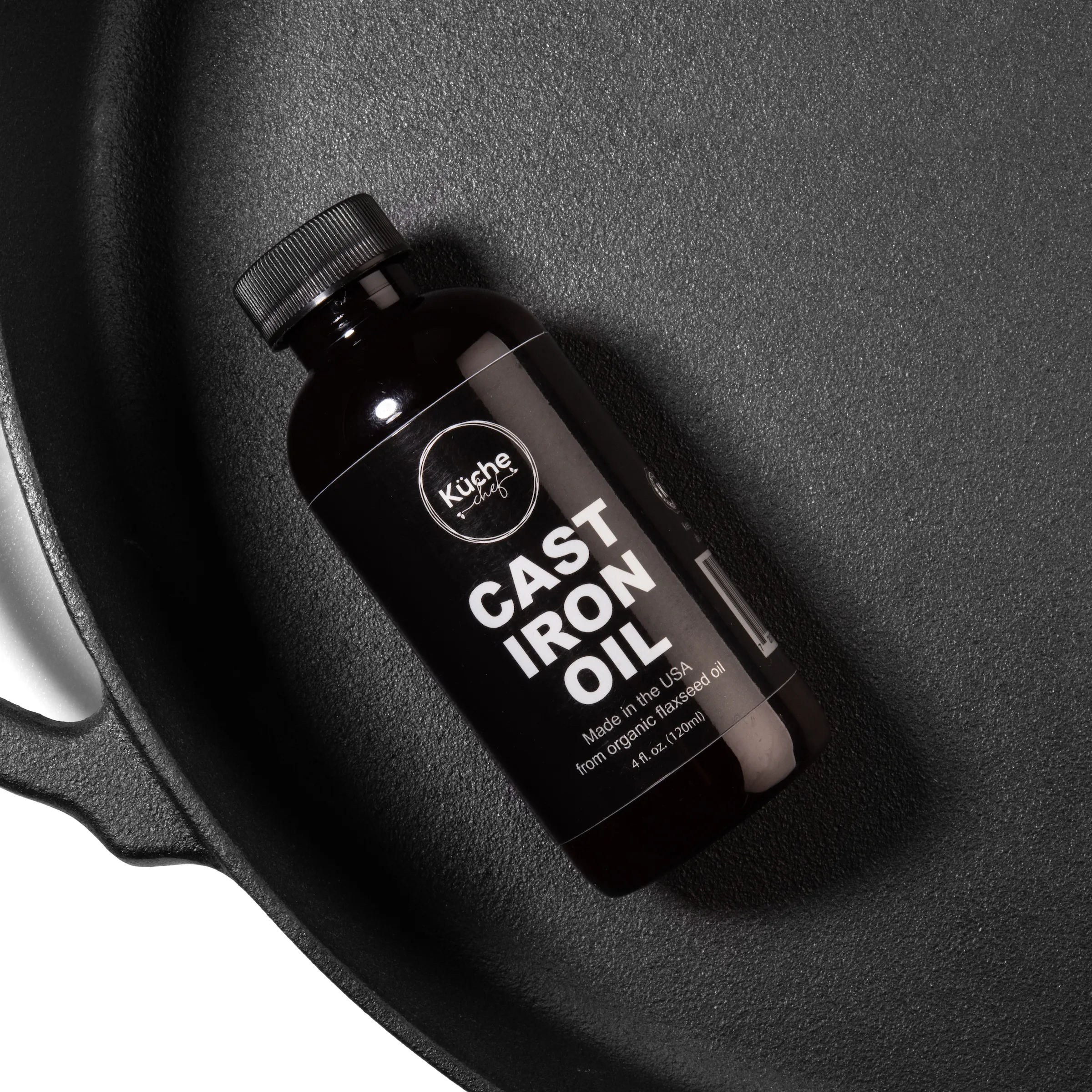 A bottle of Küche Chef Cast iron oil lying in a black cast iron skillet